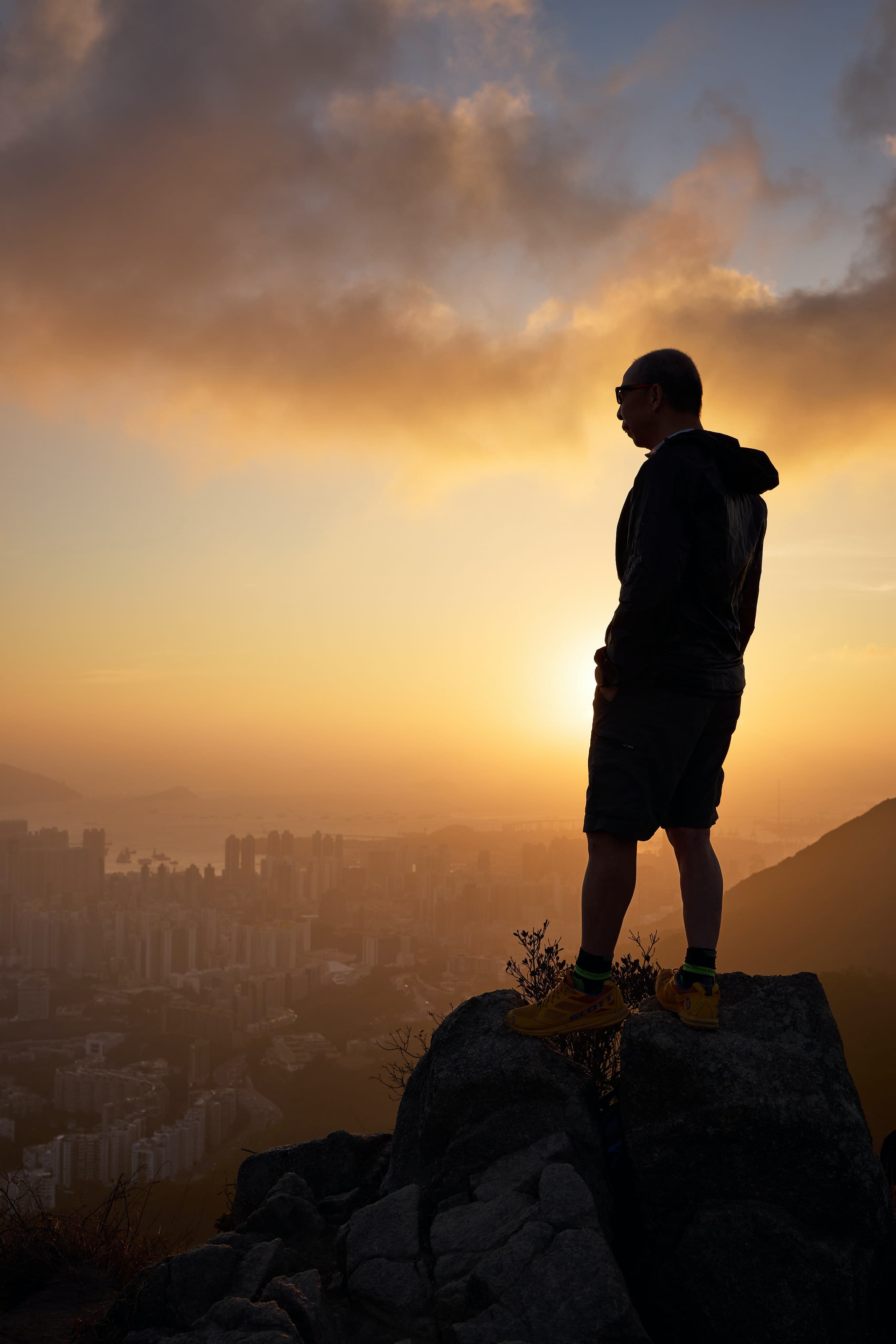 A man standing on a rock overlooking city views at dusk